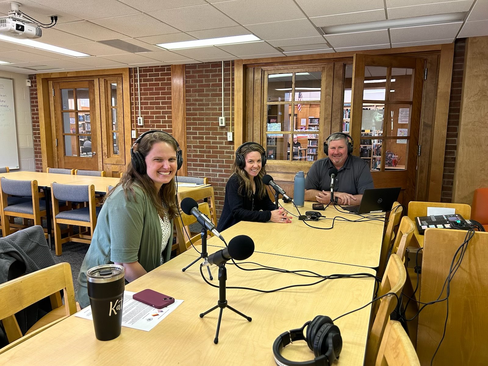 Mrs. Littlefield, Mrs. Bernard, and Mr. Konstant gather at a microphone to record a podcast. 