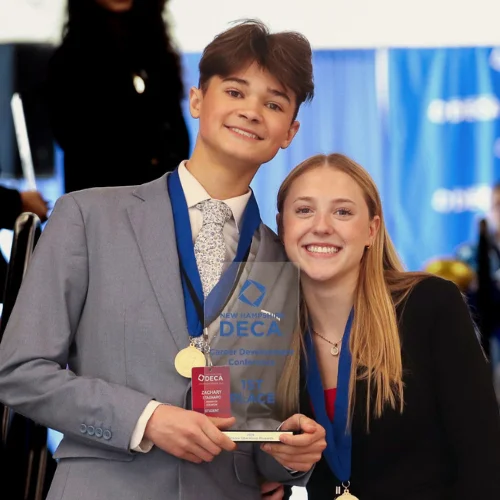 Two students smiling and posing with a DECA trophy.